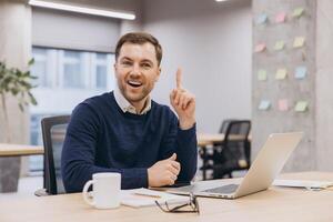 Professional businessman pointing upward while typing on laptop, expressing sudden creative breakthrough at modern workspace photo