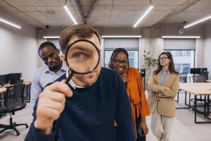 Professional diverse colleagues reviewing financial data, examining documents closely with magnifying glass in sleek workspace photo