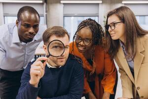 Diverse business team examining financial data through magnifying glass, collaborating in modern workplace setting photo