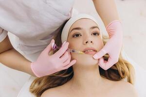 Cosmetologist injecting filler into female lips in cosmetology clinic, making botox injection for lip augmentation photo