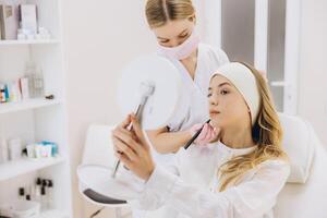 Cosmetologist marking the patient's face while she examines her reflection in the mirror, preparing for a botox injection procedure photo