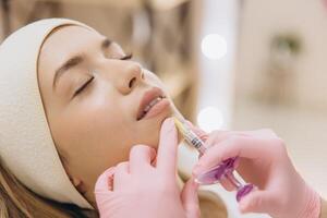 Cosmetologist injecting filler into female lips making botox injection procedure for correcting wrinkles and increasing volume in beauty salon photo