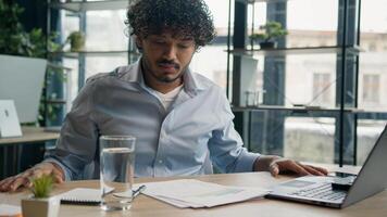Frustrated Indian business man Arabian businessman at office desk difficult work solve issue problem with paperwork documents loss finances budget trouble feel stress disappointed negative emotions photo