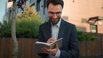 Caucasian business man businessman outside thinking writing notes in notebook university teacher professor in city hold paper notepad smile come up with idea creative thought prepare for exam studying photo