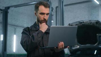Serious focused Caucasian man guy technician auto mechanic engineer check repairing car problem computer diagnostics electric automobile engine with laptop checking maintenance in garage vehicle shop photo