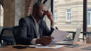 Stressed upset failure paperwork stress problem troubled African American entrepreneur with laptop report check data in papers dissatisfied mistake bad result business man office businessman male guy photo