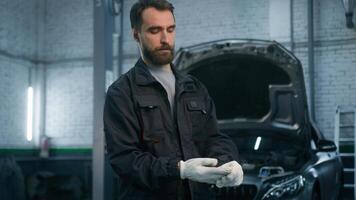 Auto mechanic taking off gloves after work automobile industrial factory. Portrait Caucasian man technician engineer worker repairman in uniform repair car service small own business vehicle service photo