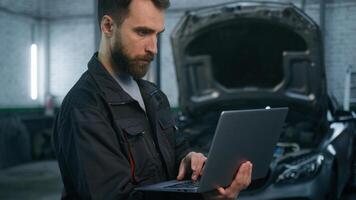 Serious focused Caucasian man guy technician auto mechanic engineer check repairing car problem computer diagnostics electric automobile engine with laptop checking maintenance in garage vehicle shop photo