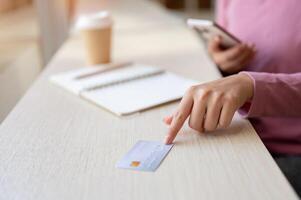 A woman sitting in a coffee shop, pointing at a credit card on the table. photo