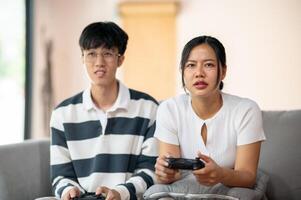 Two Asian friends excitedly play a game with joysticks in the living room, having a fun time. photo