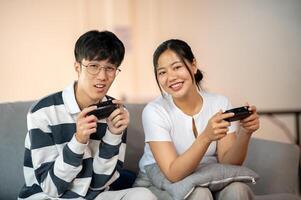 Two excited, joyful Asian friends are enjoy playing a game together on the sofa at home, having a fun time. photo