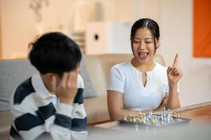 A happy Asian woman enjoys playing chess with her friend at home, explaining the chess game rules. photo