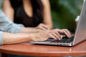 A close-up of a man typing on a laptop keyboard, working on his laptop, sitting at an outdoor table. photo