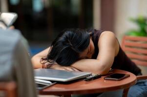 A tired, sleep-deprived Asian woman takes a nap at an outdoor table while working on her tasks. photo