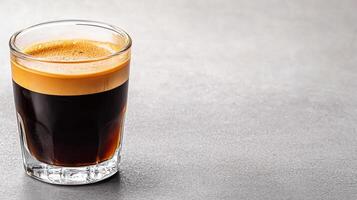 rich espresso with golden crema in glass on gray surface photo
