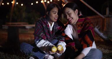 Handheld selective focus shot, Two Asian siblings enjoy talking and grilling corn while sit around a warm campfire on a chilly evening. video