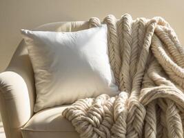 A plain white square throw pillow, placed on a cozy armchair with a textured blanket draped over it photo