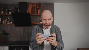 An expressive and emotional middle-aged man plays a game on his smartphone. The excitement of the game has fully captured the gamer s attention, drawing him away from his home environment. video