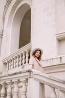woman in elegant coat and hat against an intricate architectural backdrop, harmoniously blending modern fashion with historical allure. The soft daylight adds to its timeless appeal. photo