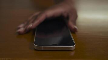 Close-up shot of smartphone on the table. African woman quickly grabs the smartphone from the table and looks at it. video