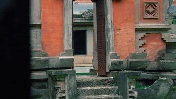 A view of an ancient temple entrance with intricate stone carvings and a weathered wooden door. The structure features a mix of red and gray stone, surrounded by lush greenery video