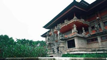 A traditional temple with intricate stone carvings and statues, surrounded by lush greenery. The architecture features ornate details and a serene atmosphere, typical of Balinese design video