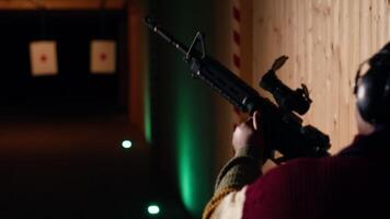 Woman in firing range training with pistol, looking at results on paper target. African american person doing shooting sport, sharpening skills, checking points scored on bullseye, camera B video