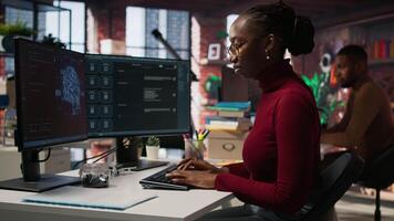 IT startup worker using large language model application to get help with coding tasks. Woman interacting with AI LLM chatbot PC GPT software on PC in software development workplace, camera A video