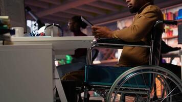 Engineer with disability coding AI algorithms in inclusive startup office using tablet, refining machine learning models. Man in wheelchair coding on device in Silicon Valley workplace, camera B video