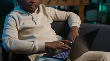 Smiling male freelancer browsing the web on laptop in a modern apartment, demonstrating a lifestyle of independence. Productivity in a virtual workspace, man multitasking. Camera A. video