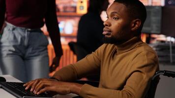 Startup cybersecurity expert in wheelchair looking for company security vulnerabilities on computer, talking with colleague. Man with disability typing on PC and chatting with coworker, camera B video