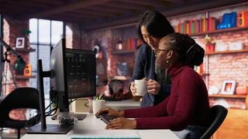 Exhausted AI startup employee rubbing forehead while analyzing datasets on computer, receiving coffee from project CTO manager to get energy and continue coding, camera B video