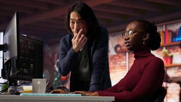 Cheerful supervisor in artificial intelligence startup enjoying laughter with worker coding applications. Happy team leader joking with employee doing code testing in relaxed workspace, camera B video