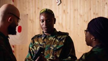 Army commander talking with recruits in shooting gallery, showing them how to reload firearms. Military officer instructing soldiers on how to load ammunition into pistol, camera B video