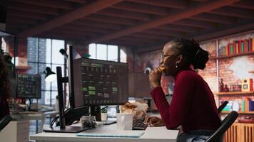 Programmer coding AI algorithm in startup, eating food at desk while refining machine learning models. Stressed woman using coding platform in Silicon Valley office and enjoying snack, camera A video