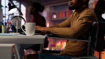 Man in wheelchair working in inclusive AI tech agency providing software development services. IT worker with disability using machine learning to streamline coding process in startup office, camera B video