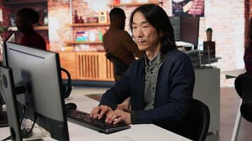 Portrait of smiling senior engineer coding advanced AI algorithm in startup office, refining machine learning models. Cheerful man using coding platform in Silicon Valley workplace, camera A video
