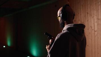 Shooting range customer shooting targets with pistol, learning to operate handgun in close quarters. Man at indoor shooting ground firing lethal fire weapon, wearing protection equipment, camera A video