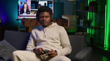 African american man plays intense online games at home, spamming attack buttons on his controller. Gamer participating in online competition, playing on gaming console. Camera A. video