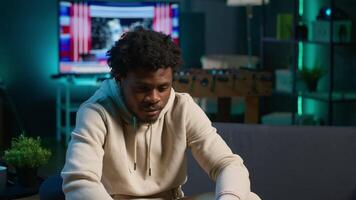 Black remote worker enjoying flexibility and comfort while browsing online on laptop in his stylish apartment decorated with neon lights. Freelance work perfectly captured in a cozy home. Camera A. video