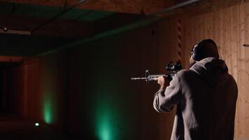 Shooting gallery client using assault rifle to hit targets, wearing protection headset. Person wearing safety earmuffs at firing range shooting bullseyes, enjoying using semiautomatic weapon video