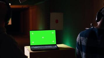 Green screen laptop in shooting range next to man successfully shooting targets. Mockup notebook next to person being congratulated by instructor for accurately hitting bullseye, camera B video