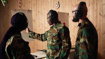 Portrait of happy army soldiers in shooting gallery looking at targets, comparing points obtained. Cheerful military units testing accuracy in firing range, looking at shot bullseye, camera A video