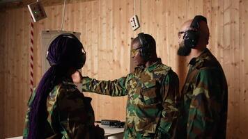 Portrait of joyous army soldiers wearing safety gear in shooting gallery, preparing to fire at targets. Smiling military units in uniform and protection equipment testing accuracy, camera A video