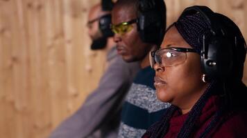 Man in firing range doing shooting sport, looking at results on paper target. Person wearing safety gear training with handgun, sharpening skills, checking points scored on bullseye, camera B video