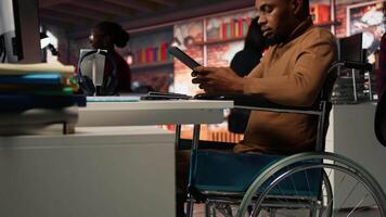 Engineer with disability coding AI algorithms in inclusive startup office using tablet, refining machine learning models. Man in wheelchair coding on device in Silicon Valley workplace, camera A video