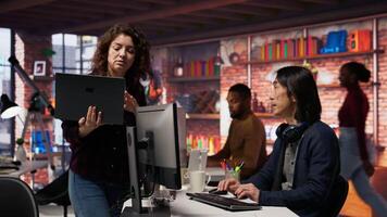 Startup intern holding laptop asks questions to senior technician coding advanced AI algorithm. Employee requests help from CTO manager in Silicon Valley workplace, camera B video