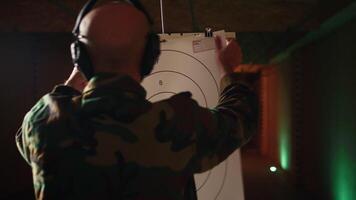 Man in firing range shooting targets with pistol, wearing earmuffs to protect hearing. Person training with weapon, hitting bullseyes, using safety gear to prevent damage from gunshots, camera A video