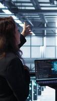 Vertical Software developers using AI tech on laptop in data center managing server virtualization. IT expert coding on notebook in server room using artificial intelligence, finetuning network, camera B video