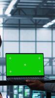 Vertical Technicians in data center using green screen mockup laptop to develop disaster recovery plans. IT specialists in server farm testing failover scenarios on chroma key device, protecting data, camera A video